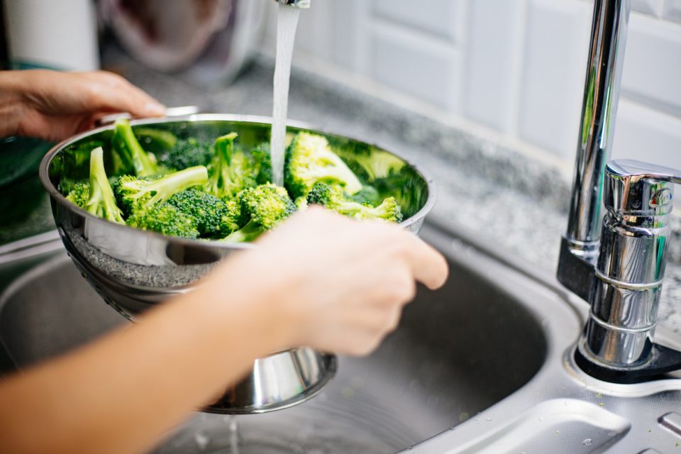 Woman washing broccoli in the kitchen sink