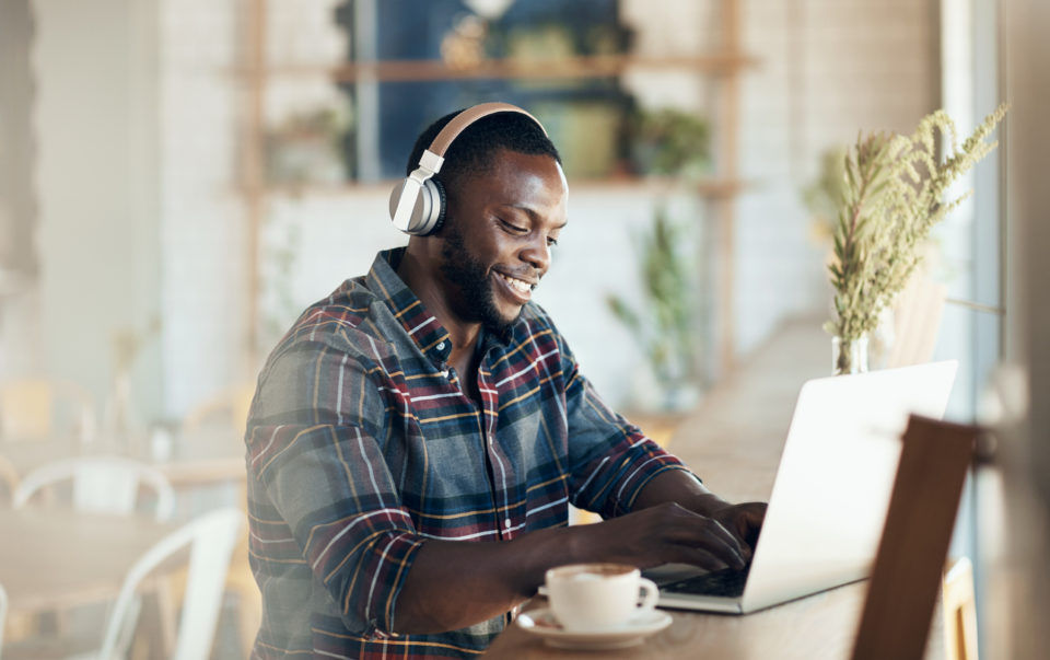 Cropped shot of a handsome young businessman wearing headphones to listen to music and using his computer in a cafe