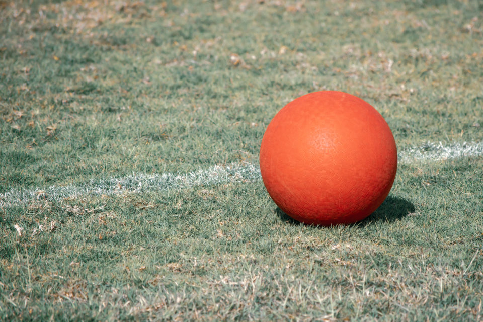 A red playground ball sits next to the white line on a green grass field.