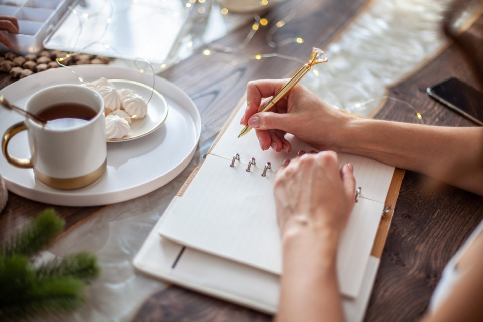 Young woman writing plans or goals for New Year 2021 while her daughter crafting Christmas trees