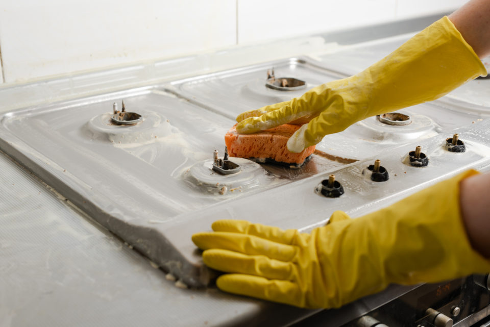 Hands in yellow gloves washing gas stove.