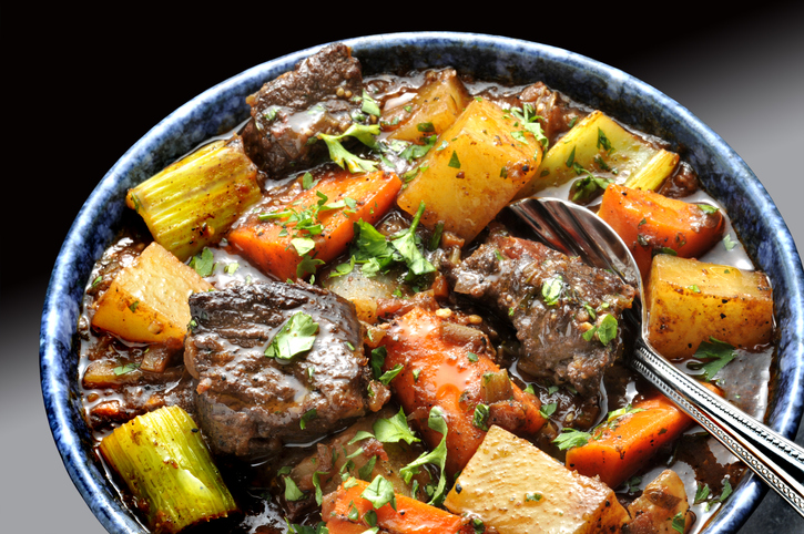 Beef stew  with carrots and potatoes n blue bowl with spoon.