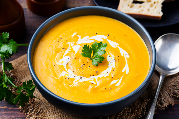 Pumpkin and carrot soup, tadka with cream and parsley on dark wooden background. Close up