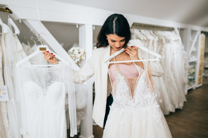 Attractive young blond woman is smiling and enjoying while choosing wedding dress in modern wedding salon.