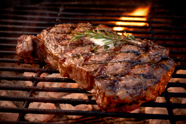 Juicy ribeye beef steak with perfect grill marks topped with Rosemary sprig and melted butter