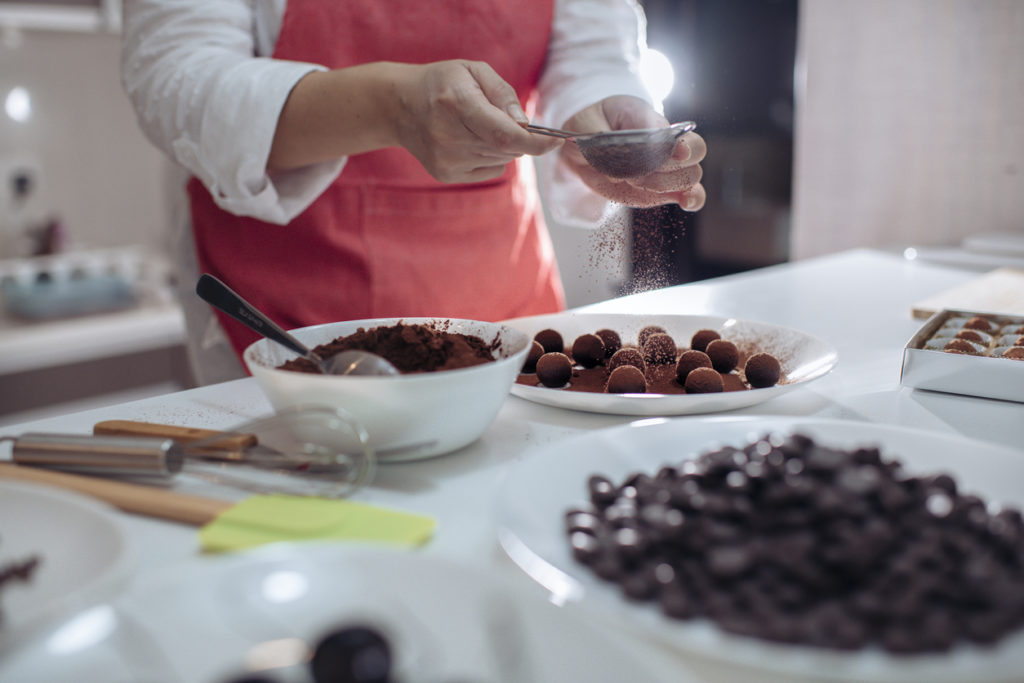 Adult female dessert chef dusting and coating chocolate truffles in the kitchen