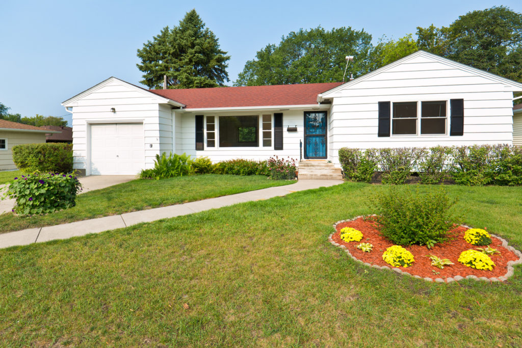 A 1950s mid-century modern bungalow style house in the United States. The real estate featuring attached garage, picture windows and a well landscaped front yard and driveway.