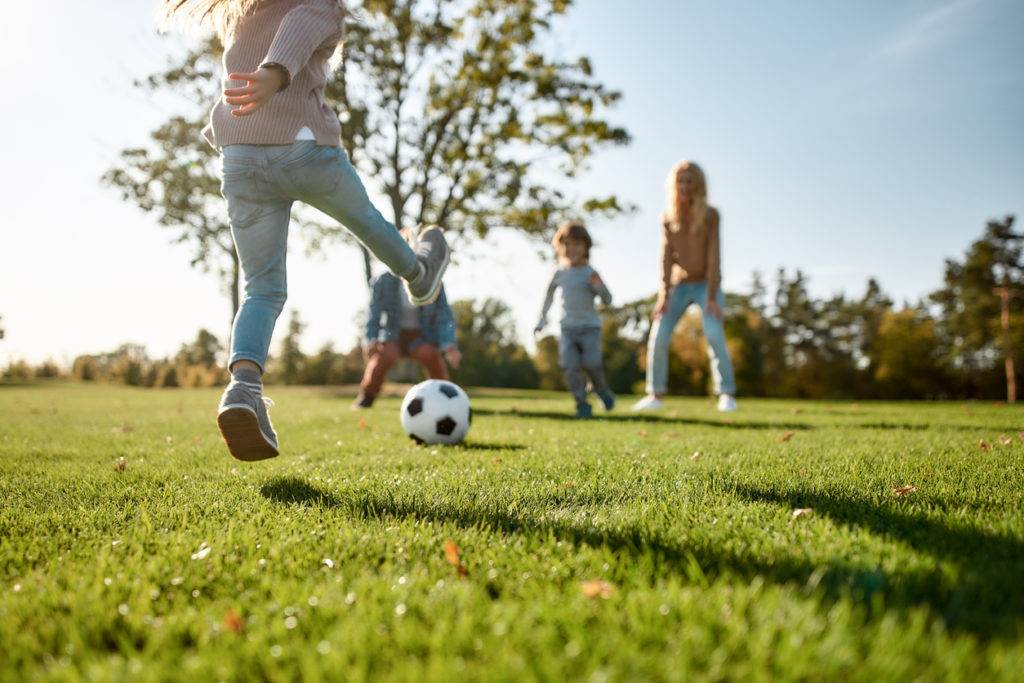 Family playing soccer at park outdoors.