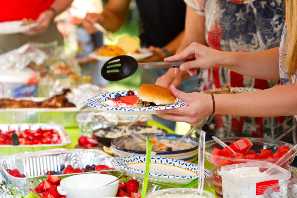 Guests filling plates at a summer potluck barbeque